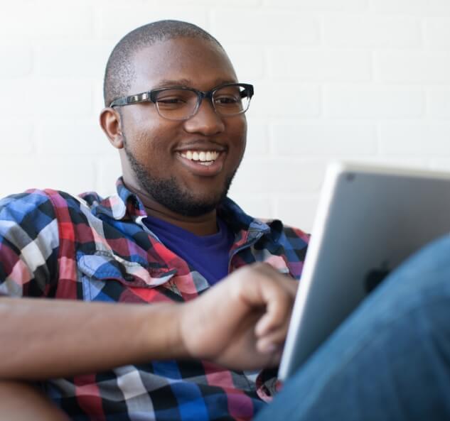 Young man smiling at tablet while seated.