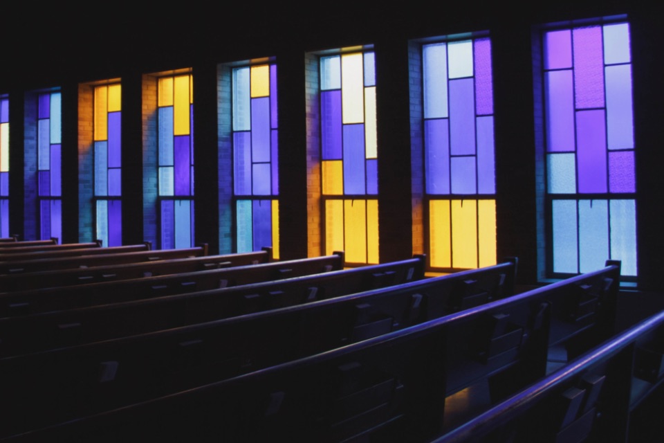 Inside of traditional church with simple stained glass and pews.